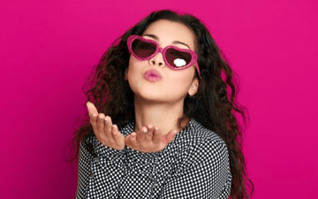 Woman with heart shaped glasses blows a kiss
