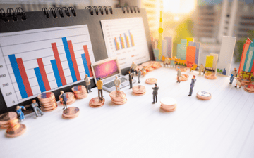 Miniature figures stand on pennies looking at charts 
